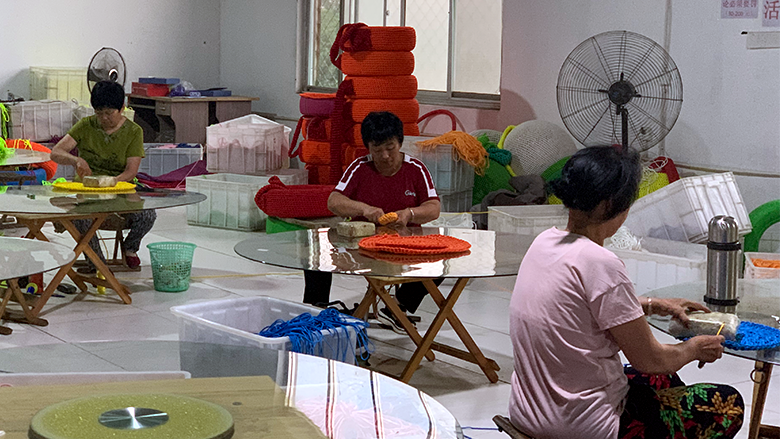 Three people sit at tables weaving in a Taobao village in China